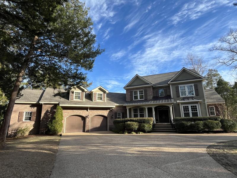 A large brick home with a driveway and trees, showcasing a 3D animated roof design in New Jersey.